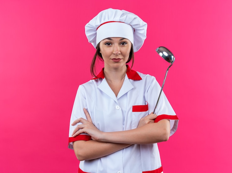 Foto grátis jovem cozinheira confiante vestindo uniforme de chef e segurando uma concha, cruzando as mãos isoladas na parede rosa