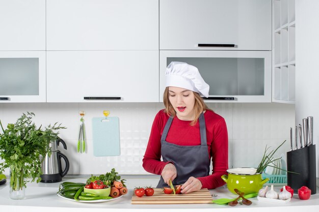 Jovem cozinheira de avental cortando tomates