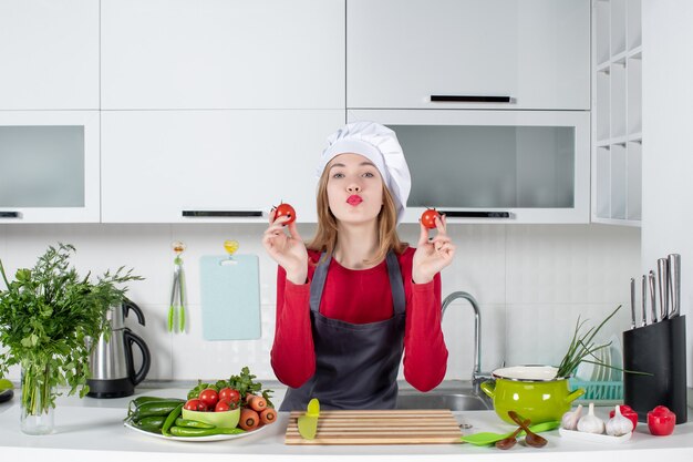 Jovem cozinheira de avental segurando tomates e mandando beijo de frente