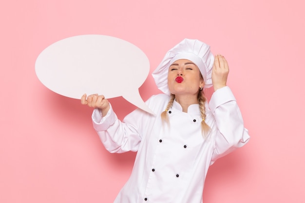 Jovem cozinheira de terno branco segurando uma placa branca no cozinheiro rosa