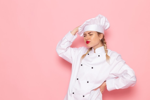 Foto grátis jovem cozinheira em traje de cozinha branco, de frente, apenas posando com uma expressão confusa no cozinheiro rosa