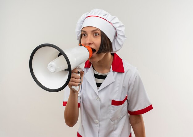 Jovem cozinheira impressionada com uniforme de chef falando por alto-falante, olhando para o lado isolado no branco com espaço de cópia