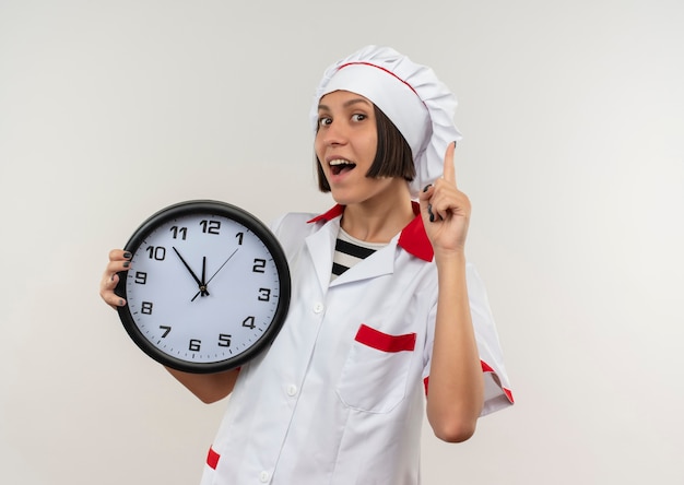 Jovem cozinheira impressionada com uniforme de chef segurando o relógio e levantando o dedo isolado no branco com espaço de cópia