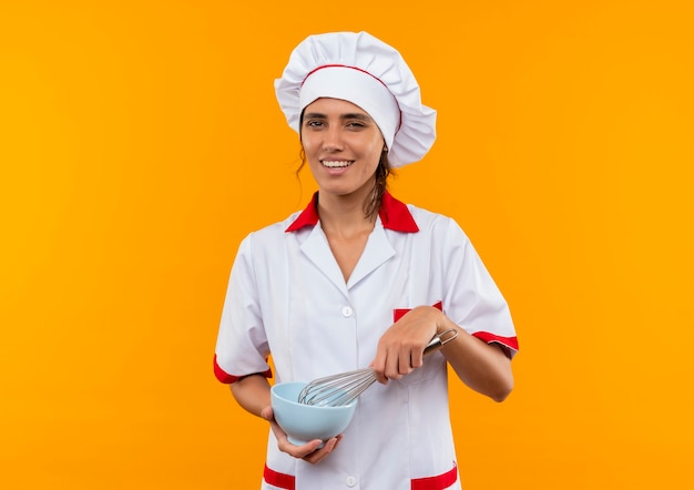 Foto grátis jovem cozinheira sorridente usando uniforme de chef segurando a tigela e batedor com espaço de cópia