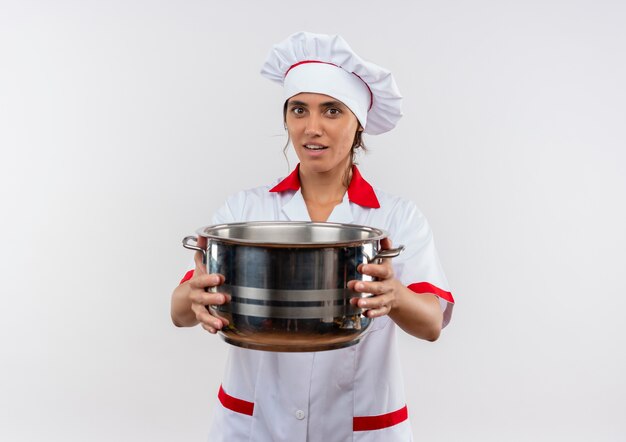 Jovem cozinheira sorridente usando uniforme de chef segurando uma panela para a câmera com espaço de cópia