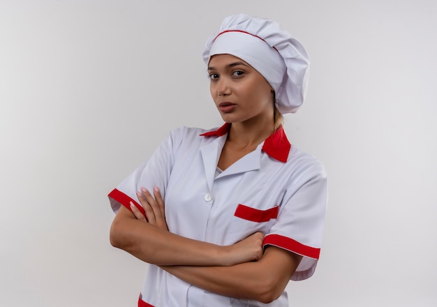 jovem cozinheira usando uniforme de chef cruzando as mãos na parede branca isolada com espaço de cópia