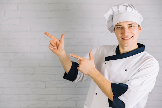 Jovem cozinheiro apontando os dedos em algum lugar