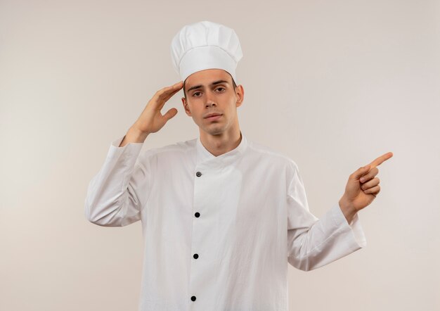 Jovem cozinheiro cansado vestindo uniforme de chef, colocando a mão na testa apontando o dedo para o lado com o espaço da cópia