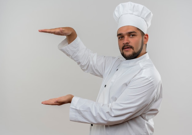 Jovem cozinheiro com uniforme de chef mostrando tamanho olhando