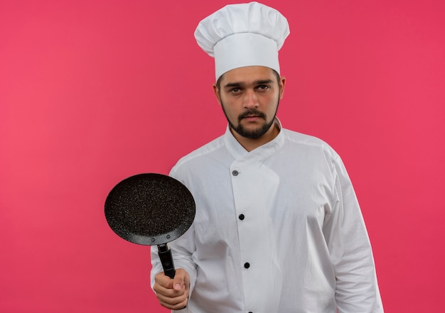 Jovem cozinheiro com uniforme de chef segurando uma frigideira, parecendo isolado no espaço rosa