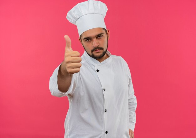 Jovem cozinheiro confiante com uniforme de chef, mostrando o polegar isolado na parede rosa com espaço de cópia