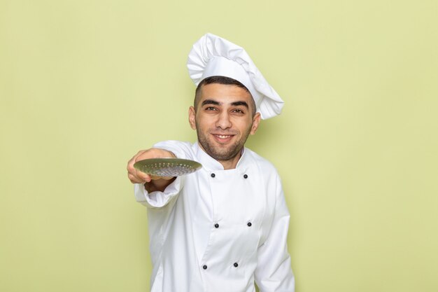 Jovem cozinheiro masculino de terno branco apontando para a colher de prata no verde