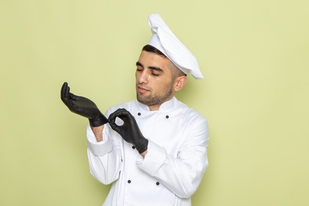 Jovem cozinheiro masculino em traje de cozinha branco e luvas escuras verde