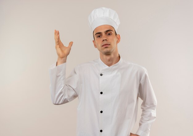Jovem cozinheiro masculino vestindo uniforme de chef fingindo estar segurando algo na parede branca isolada com espaço de cópia
