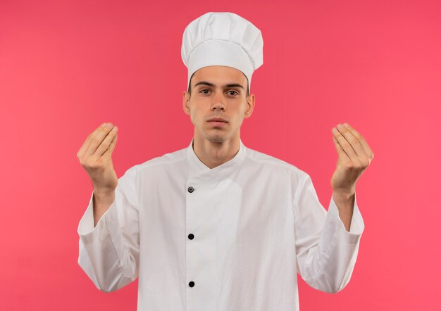 jovem cozinheiro masculino vestindo uniforme de chef mostrando gesto de ponta na parede rosa isolada