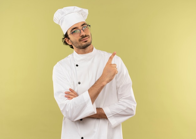 jovem cozinheiro satisfeito vestindo uniforme de chef e óculos apontando para o lado