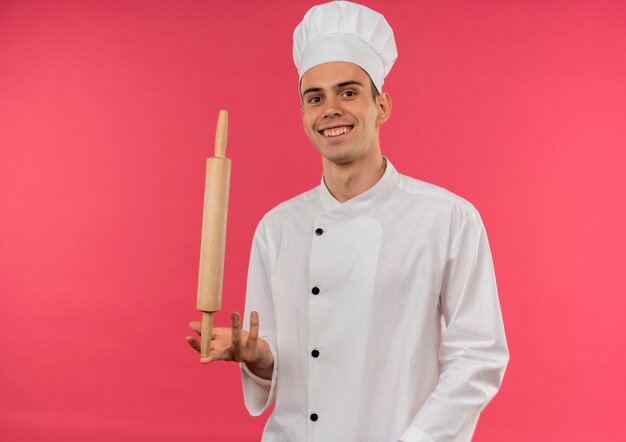 Jovem cozinheiro sorridente usando uniforme de chef e segurando o rolo de massa no dedo