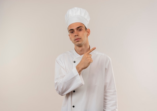 jovem cozinheiro usando uniforme de chef aponta dedo para lado na parede branca isolada com espaço de cópia