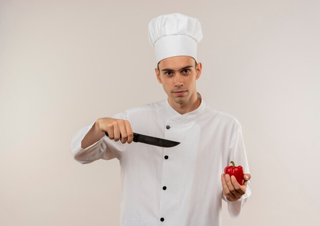 jovem cozinheiro usando uniforme de chef aponta faca para apimentar na mão na parede branca isolada com espaço de cópia