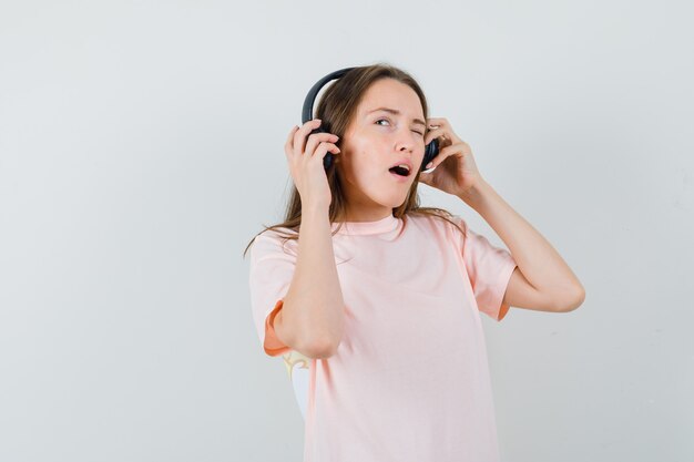 Jovem curtindo música com fones de ouvido em uma camiseta rosa e olhando pensativa. vista frontal.