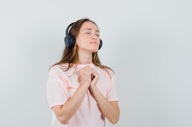 Jovem curtindo música com fones de ouvido em uma camiseta rosa e parecendo em paz. vista frontal.