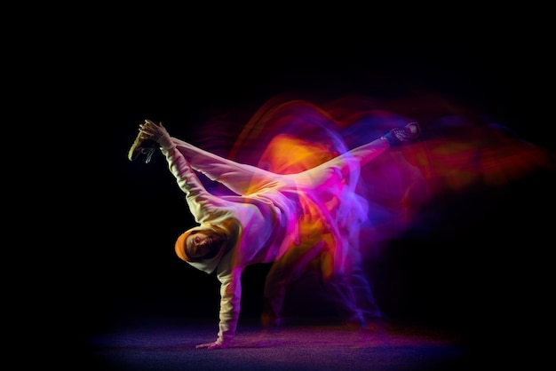 Jovem dançando hiphop breakdance isolado sobre fundo preto em neon com luzes mistas Foto Premium
