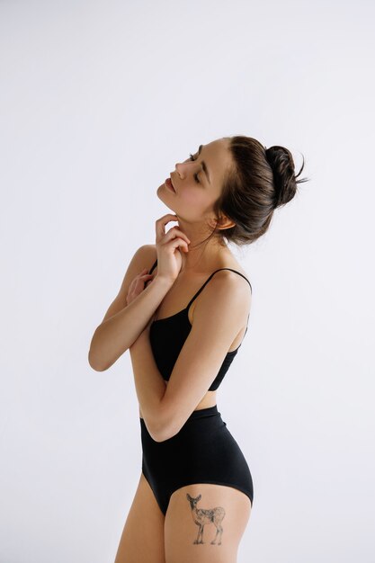Jovem dançarina de balé em macacão preto contra a parede branca do estúdio