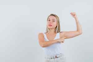 Foto grátis jovem de blusa branca apontando para os músculos do braço e parecendo focada