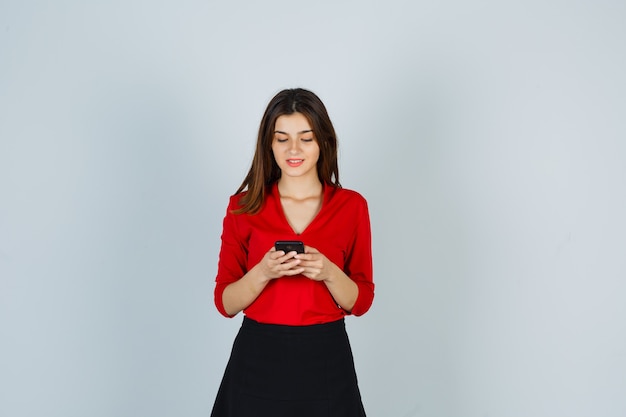 Foto grátis jovem de blusa vermelha, saia, conversando no celular e parecendo feliz