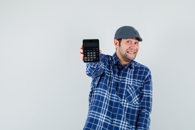 Jovem de camisa, boné mostrando calculadora e olhando alegre, vista frontal.