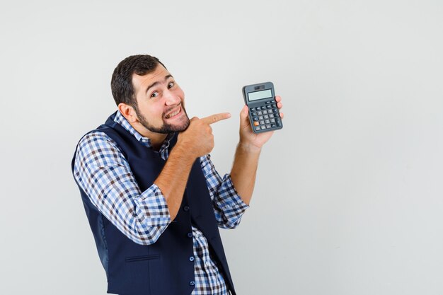 Jovem de camisa, colete apontando para a calculadora e parecendo alegre