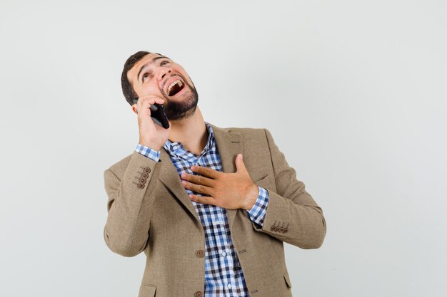 Jovem de camisa, jaqueta, falando no celular e parecendo feliz, vista frontal.