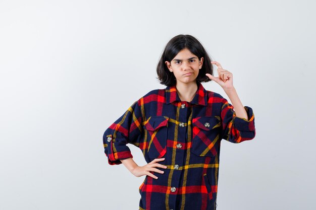 Jovem de camisa quadrada, segurando a mão na cintura enquanto estica a mão como segurando algo imaginário e olhando com foco, vista frontal.