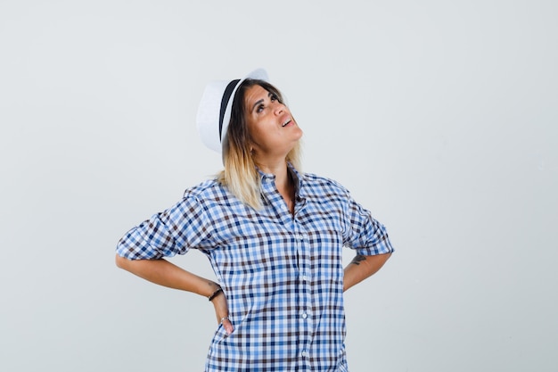 Foto grátis jovem de camisa quadriculada, olhando para cima com as mãos na cintura e parecendo confusa.