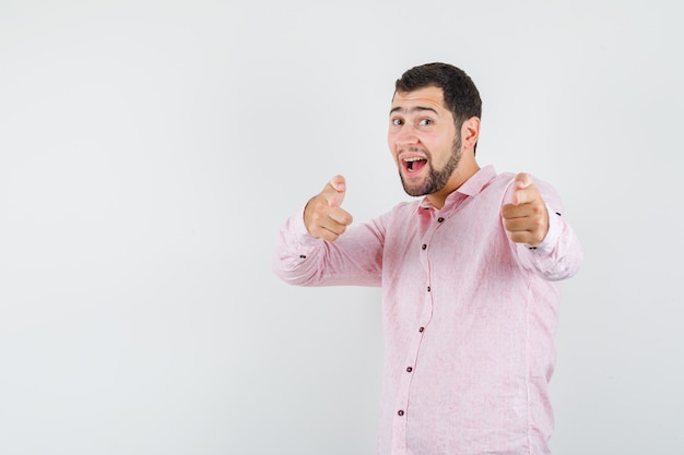 Jovem de camisa rosa apontando para a câmera e parecendo otimista