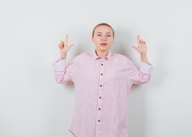 Jovem de camisa rosa apontando para cima e parecendo confiante