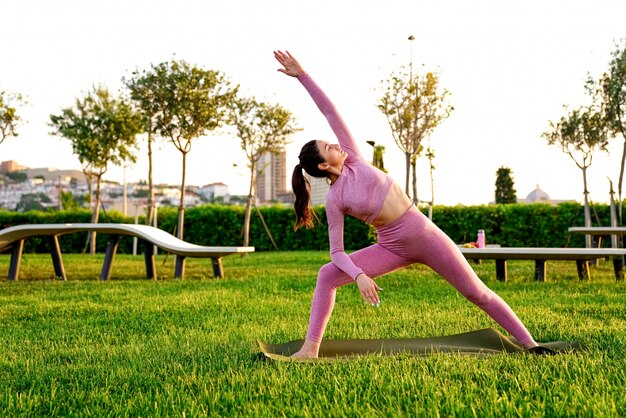 jovem de camisa rosa e calças na grama dentro do parque verde, meditando e fazendo yoga em poses diferentes