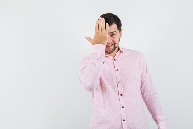 Jovem de camisa rosa segurando a mão em um olho e parecendo tímido