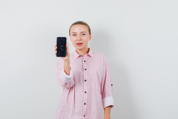 Jovem de camisa rosa segurando um celular e parecendo satisfeita