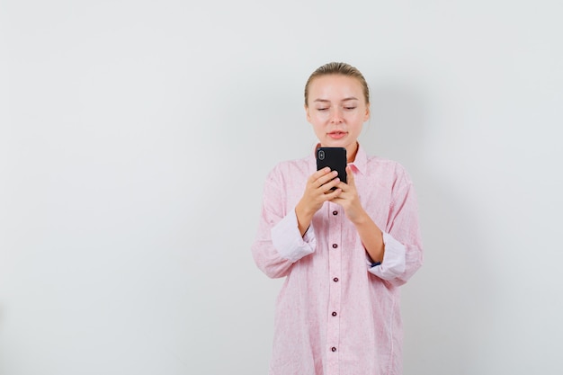 Jovem de camisa rosa usando um celular e parecendo ocupada