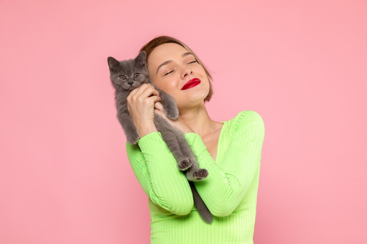 Foto grátis jovem de camisa verde e calça cinza segurando um gatinho cinza fofo