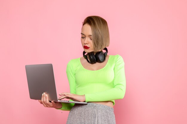 jovem de camisa verde e saia cinza usando laptop e ouvindo música
