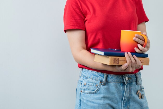 Jovem de camisa vermelha segurando livros e um copo de bebida