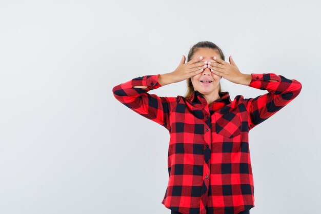 Jovem de camisa xadrez de mãos dadas nos olhos e parecendo feliz