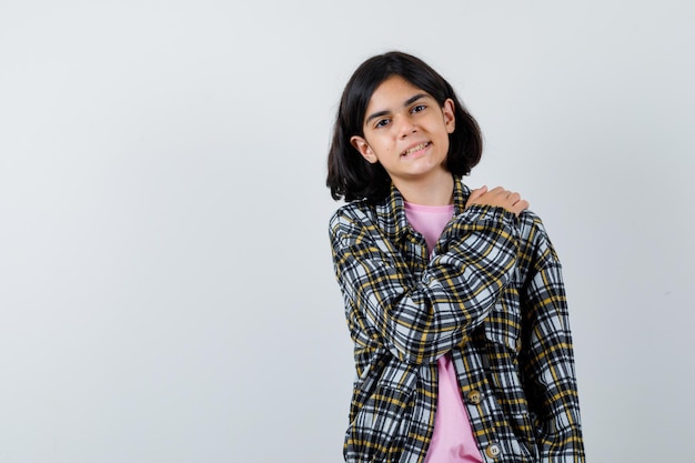 Jovem de camisa xadrez e camiseta rosa, colocando a mão no ombro e olhando bonita, vista frontal.