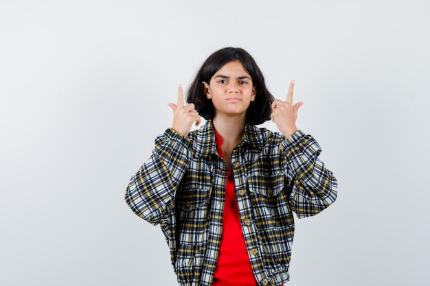 Jovem de camisa xadrez e camiseta vermelha apontando para cima e olhando bonita, vista frontal.