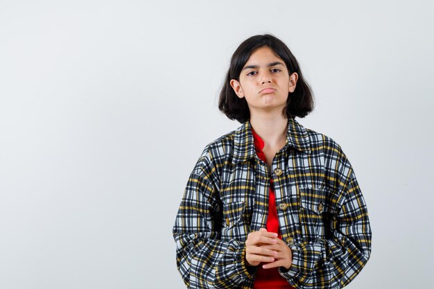 Jovem de camisa xadrez e camiseta vermelha, esfregando as mãos e olhando séria, vista frontal.