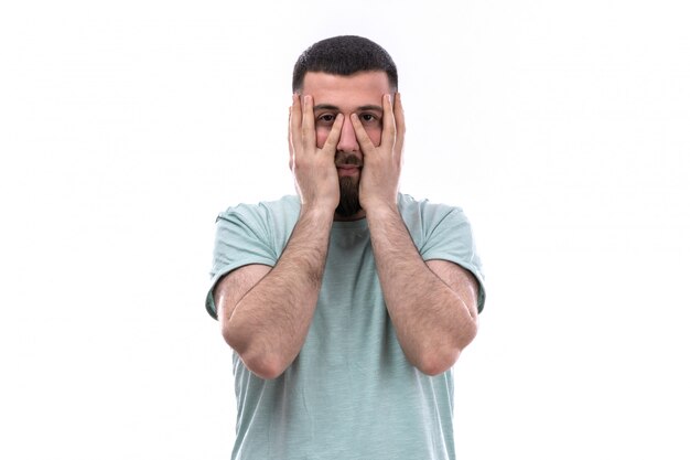 Jovem de camiseta azul com barba com as mãos ao redor do rosto