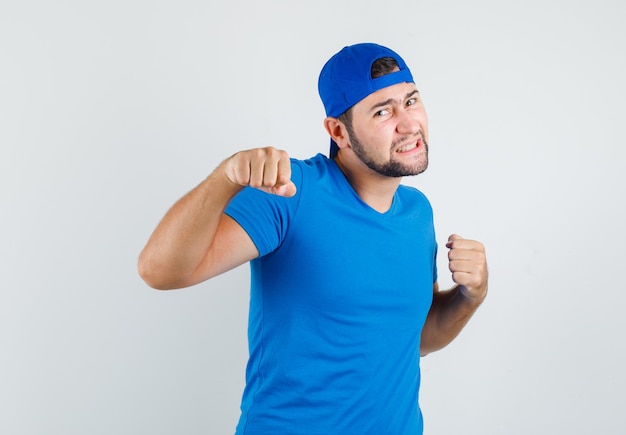 Jovem de camiseta azul e boné em pose de luta e parecendo briguento