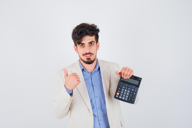 Foto grátis jovem de camiseta azul e paletó branco segurando uma calculadora, mostrando o polegar e parecendo amável
